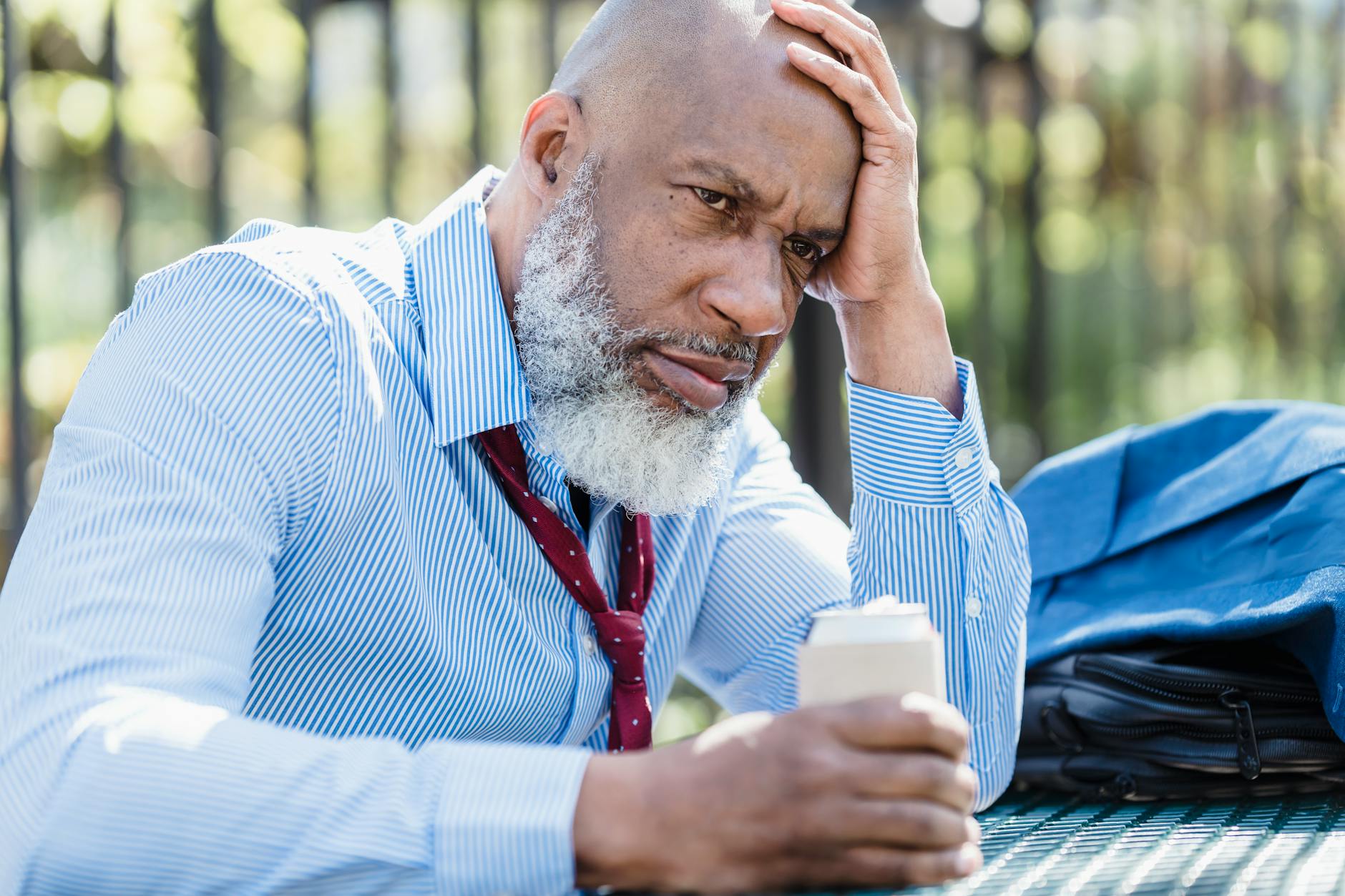 sad black businessman with alcohol drink on street